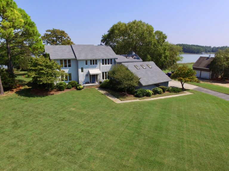 white and gray house near a grass field and body of water