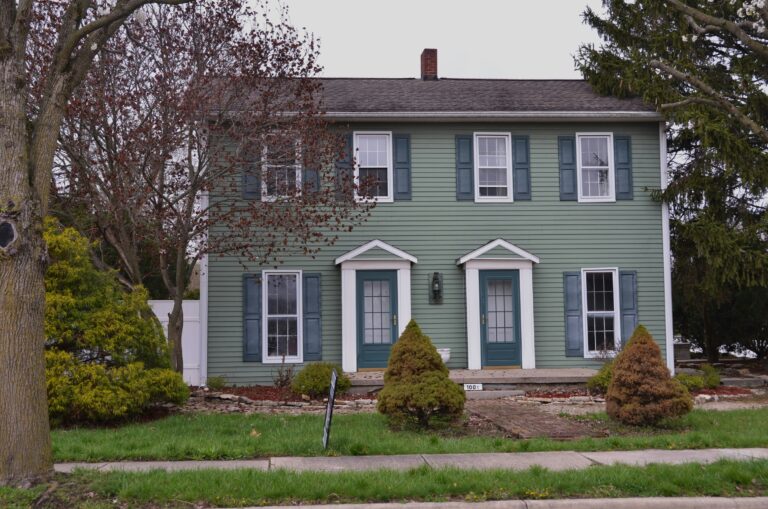 a green house with blue shutters and trees