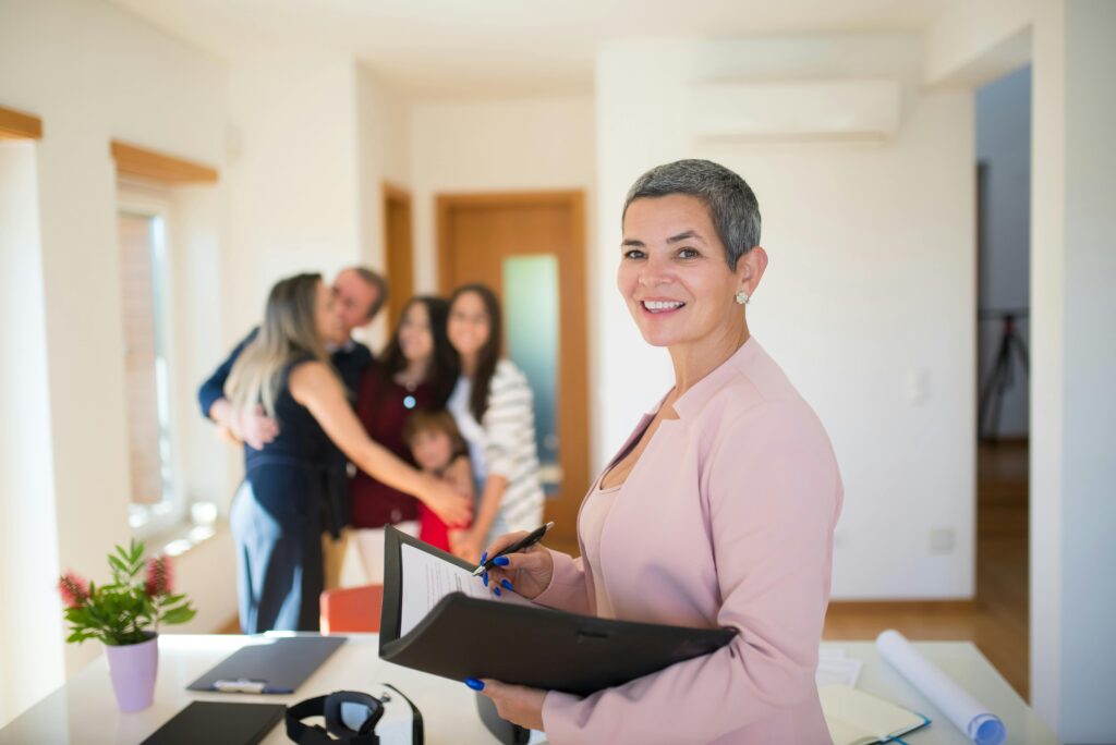 Real Estate Agent holding documents and a family hugging in the background