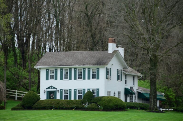 a large white historic house surrounded by mature trees and green field